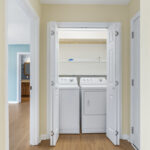 Convenient hallway laundry closet featuring side-by-side washer and dryer and overheard storage racks..